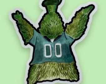 May include: A green, fuzzy, cartoon creature wearing a green jersey with the number "00" on it. The creature has a green hat and is raising its arms in the air.