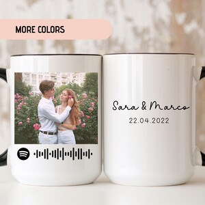 May include: Two white ceramic mugs with black handles. One mug features a photo of a couple in a garden setting with a black and white Spotify barcode. The other mug has the text "Sara & Marco" and "22.04.2022" in black.
