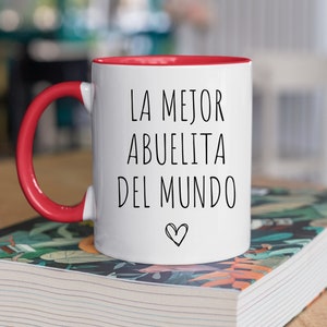 May include: White ceramic mug with a red rim and handle. The mug has black text that reads "LA MEJOR ABUELITA DEL MUNDO" with a small heart symbol.