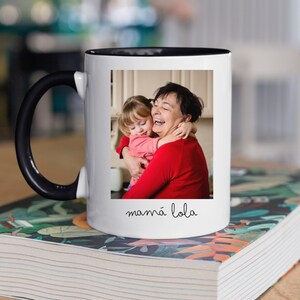 May include: White ceramic mug with a black handle and a black rim. The mug features a photo of a grandmother and granddaughter hugging, with the text "mamma lola" written below the photo.