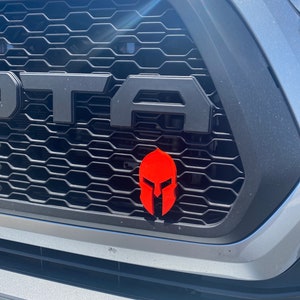 May include: A silver pickup truck with a black grille and a red Spartan helmet emblem.