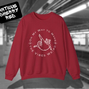 May include: Red sweatshirt with a white graphic of a raccoon with the text "On my way to make the vibes weird".