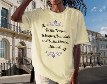 Könnte beinhalten: Hellgelbes T-Shirt mit dem Text "Tis the Season. Whispers, Scandals and Stolen Glances Abound." Das Shirt zeigt zwei Hummel-Grafiken und dekorative lila Verzierungen.