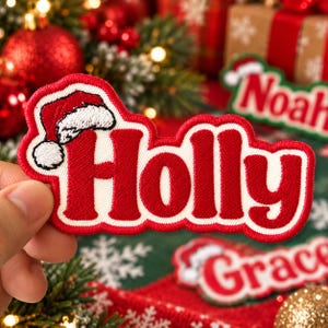 Puede incluir: Un parche bordado en rojo y blanco con el nombre Holly en letras rojas gruesas con un borde blanco. Un pequeño gorro de Papá Noel rojo y blanco está colocado sobre la letra H. El parche tiene un borde rojo grueso y una superficie texturizada.