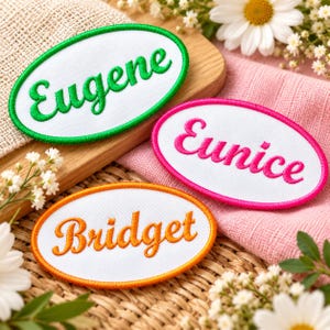 May include: Three oval-shaped embroidered patches with white fabric centers and stitched borders. One patch has a green border and the name Eugene in green, one has a pink border and the name Eunice in pink, and one has an orange border and the name Bridget in orange.