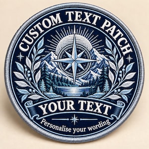 Op de afbeelding: Een ronde geborduurde patch met een donkerblauwe achtergrond, voorzien van een wit kompasroos, bergketen en boslandschap. De tekst CUSTOM TEXT PATCH staat bovenaan, met YOUR TEXT en Personalise your wording daaronder.