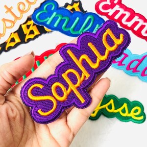 May include: Purple iron-on patch with the name "Sophia" embroidered in yellow thread.