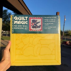 May include: A Quilt Magic no sew wall hanging kit featuring a yellow foam board with a laser-cut teddy bear design. The packaging includes the text Quilt Magic, No Sew Wall Hanging Kit, and #403 Teddy Bear, along with instructions for use.