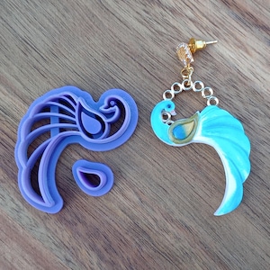 May include: A purple plastic peacock cookie cutter and a blue and gold peacock earring.