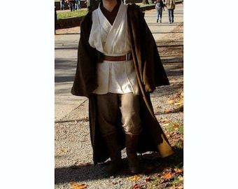 May include: A brown Jedi costume consisting of a long robe, tunic, pants, and boots. The costume includes a light-colored tunic, a brown belt, and dark brown boots. The robe is draped over the shoulders, and the pants are a lighter brown color.