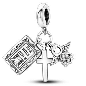 K&ouml;nnte beinhalten: Ein silberner Charm mit religi&ouml;sen Symbolen. Der Charm zeigt ein kleines offenes Buch mit dem Text "HOLY BIBLE", ein Kreuz und einen Engel mit Strasssteinen. Der Charm ist an einer silbernen Schlaufe befestigt.
