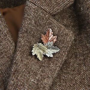 Può includere: Spilla a forma di foglie nei toni del rame, argento e oro, appuntata su una giacca di tweed marrone a spina di pesce. La spilla presenta dettagliati disegni di foglie, aggiungendo un tocco di eleganza ispirata alla natura.
