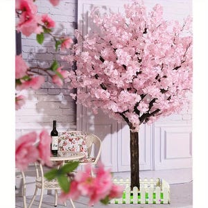 Könnte beinhalten: Ein rosa Kirschbaum mit braunem Stamm und weißem Zaunfuß. Vor dem Baum steht eine kleine weiße Tisch- und Stuhlgarnitur mit einem Blumengemuster Kissen. Auf dem Tisch steht eine Weinflasche.