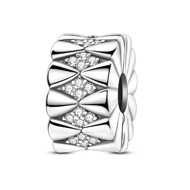 K&ouml;nnte beinhalten: Ein silberfarbener Charm-Anh&auml;nger mit einem sich wiederholenden Muster aus bogenf&ouml;rmigen Elementen und rautenf&ouml;rmigen Clustern aus kleinen, klaren Edelsteinen. Der zylindrische Charm hat ein Loch in der Mitte und ist f&uuml;r Armb&auml;nder oder Halsketten geeignet.