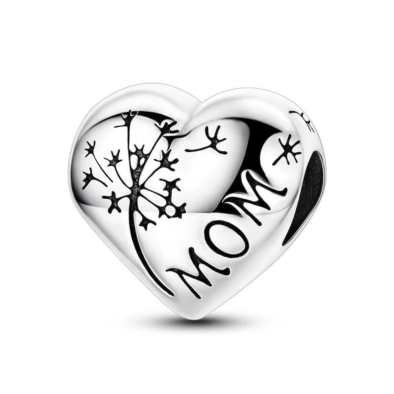 K&ouml;nnte beinhalten: Ein silberner herzf&ouml;rmiger Anh&auml;nger mit dem Wort "MOM" und einem Pusteblumen-Design. Der Anh&auml;nger ist hochglanzpoliert und reflektiert das Licht, mit den filigranen Details der Pusteblume in Schwarz.