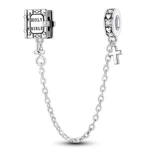 K&ouml;nnte beinhalten: Silberne Charm-Armband-Sicherheitskette mit einem Holy Bible-Charm und einem Charm mit Herzen und klaren Steinen. Ein kleiner Kreuz-Charm h&auml;ngt an dem Charm mit Herzen. Die Kette verbindet die Charms.