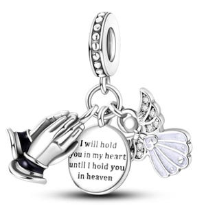 K&ouml;nnte beinhalten: Silberner Charm mit betenden H&auml;nden, einem Engel und einem runden Anh&auml;nger. Der Anh&auml;nger tr&auml;gt die Aufschrift "I will hold you in my heart until I hold you in heaven". Der Engel hat wei&szlig;e Fl&uuml;gel und Kristalle.