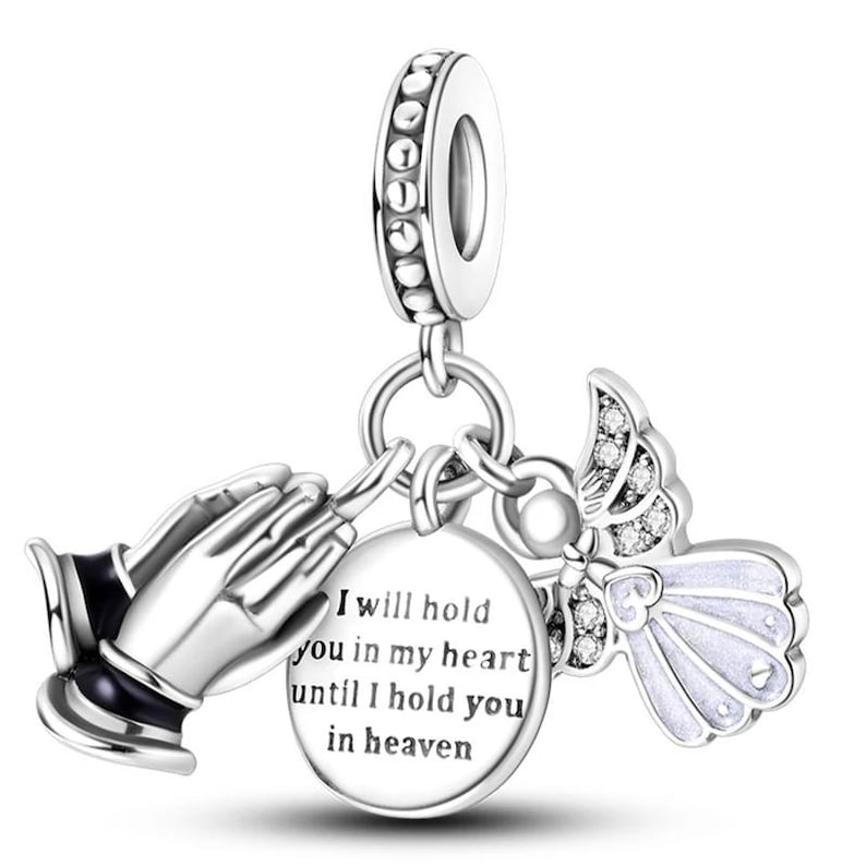 K&ouml;nnte beinhalten: Silberner Charm mit betenden H&auml;nden, einem Engel und einem runden Anh&auml;nger. Der Anh&auml;nger tr&auml;gt die Aufschrift "I will hold you in my heart until I hold you in heaven". Der Engel hat wei&szlig;e Fl&uuml;gel und Kristalle.