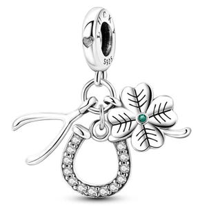 K&ouml;nnte beinhalten: Ein silberner Charm mit einem Kleeblatt, einem Hufeisen und einem Wunschknochen-Design. Das Hufeisen ist mit kleinen, klaren Steinen besetzt. Das Kleeblatt hat einen gr&uuml;nen Mittelstein. Der Charm hat eine Schlaufe mit dem Wort "LUCK" und den Buchstaben "S925".