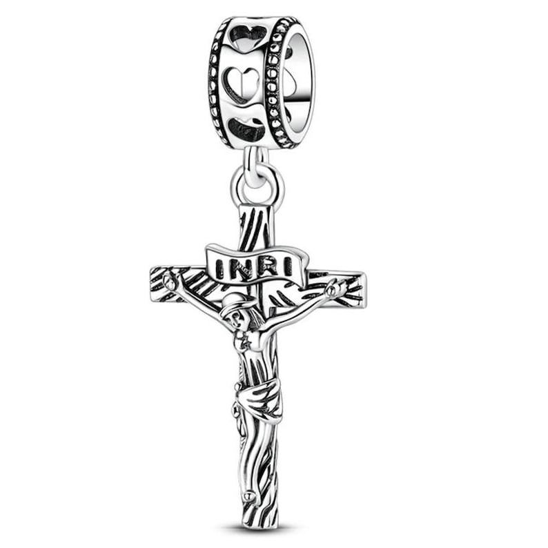 K&ouml;nnte beinhalten: Ein silberfarbener Charm-Anh&auml;nger mit einem Kreuzigungsdesign. Der Anh&auml;nger zeigt Jesus am Kreuz, mit den Buchstaben INRI auf einem Banner. Der obere Teil des Anh&auml;ngers hat einen Ring mit herzf&ouml;rmigen Ausschnitten.
