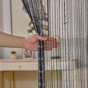 May include: Black beaded curtain with clear beads hanging from the strings. The curtain is made of thin, black strings with clear beads spaced evenly along the strings.