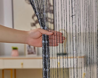 May include: Black beaded curtain with clear beads hanging from the strings. The curtain is made of thin, black strings with clear beads spaced evenly along the strings.