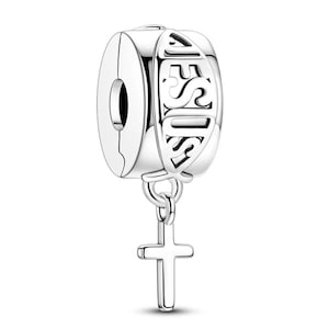 K&ouml;nnte beinhalten: Ein silberner Charm-Anh&auml;nger mit dem Wort &bdquo;JESUS&ldquo; auf der Seite ausgeschnitten. Ein kleines Kreuz h&auml;ngt von unten. Der Charm-Anh&auml;nger ist f&uuml;r ein Armband oder eine Halskette gedacht.