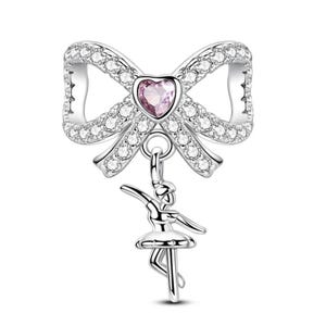 K&ouml;nnte beinhalten: Silberner Charm mit einem Bogen-Design, besetzt mit klaren Kristallen und einem rosa herzf&ouml;rmigen Edelstein. Ein Ballerina-Charm h&auml;ngt darunter.