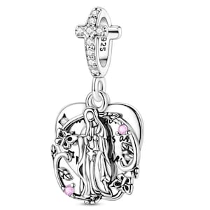 K&ouml;nnte beinhalten: Ein silberner Charm-Anh&auml;nger mit einem Kreuz an der Spitze, verziert mit klaren Kristallen. Der Charm-Anh&auml;nger hat einen herzf&ouml;rmigen Anh&auml;nger mit einer religi&ouml;sen Figur, floralen Akzenten und rosa Edelsteinen. Der Anh&auml;nger ist mit aufwendigen Designs und der Zahl "925" versehen.