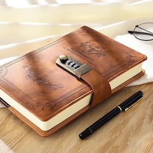 May include: Brown leather journal with a combination lock and the text "DETERMINATION IS THE BEGINNING OF SUCCESS." The journal has decorative floral patterns and a matching leather strap. A black pen rests beside the journal.