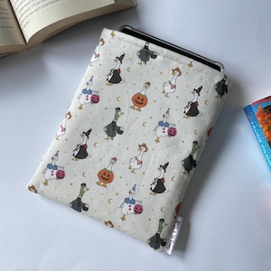 May include: Cream tablet sleeve featuring a repeating pattern of geese in Halloween costumes. The geese are dressed as witches, pumpkins, and clowns. The sleeve is designed to hold a tablet and has a soft interior.