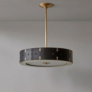 Puede incluir: Una moderna lámpara colgante circular. La pantalla negra tiene detalles dorados en forma de ojo de cerradura y un borde dorado. Se suspende de una varilla y un soporte de techo dorados.