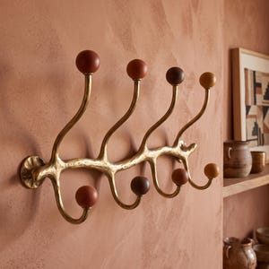 May include: A wall-mounted coat rack featuring a textured, branch-like brass frame with eight curved hooks. Each hook terminates in a smooth, spherical knob in varying shades of brown, ranging from light tan to deep chocolate and terracotta.