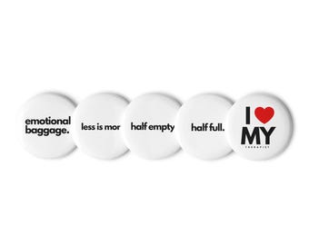 Può includere: Cinque bottoni rotondi bianchi con testo nero. I bottoni recitano: "emotional baggage.", "less is mor", "half empty", "half full.", e "I ❤️ MY THERAPIST". Il cuore è rosso.