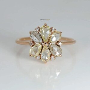 May include: A rose gold ring with a flower-shaped design featuring a cluster of pear-shaped diamonds. The diamonds are a mix of clear and yellow.