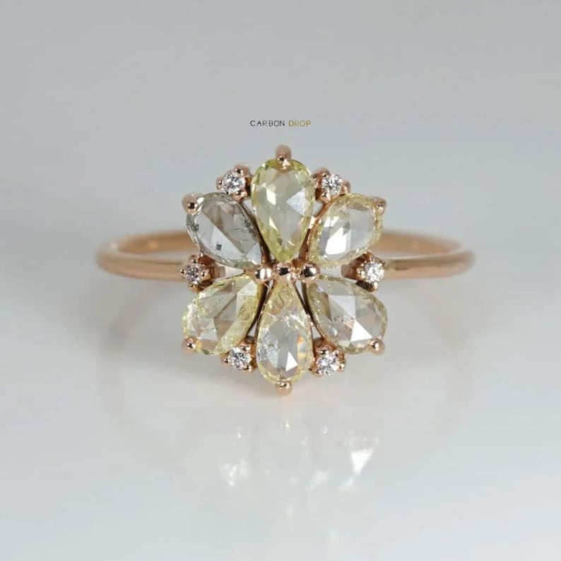 May include: A rose gold ring with a flower-shaped design featuring a cluster of pear-shaped diamonds. The diamonds are a mix of clear and yellow.