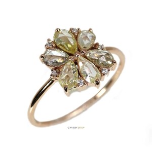 May include: A rose gold ring with a flower-shaped design featuring six pear-shaped diamonds. The diamonds are a mix of clear and yellow.