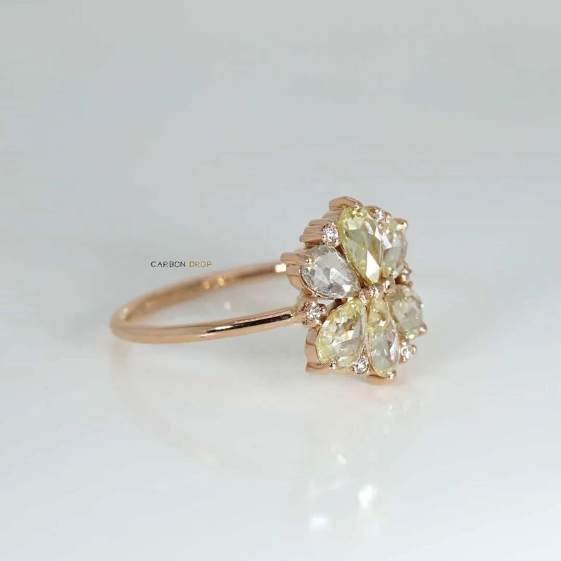 May include: A rose gold ring with a flower-shaped design featuring a cluster of pear-shaped diamonds. The diamonds are a mix of clear and yellow.