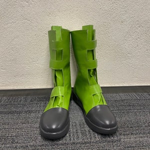 May include: A pair of green leather boots with black toes and buckles. The boots are tall and have a slightly pointed toe.
