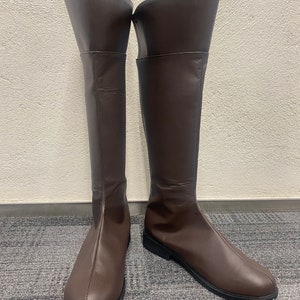 May include: A pair of brown leather knee-high boots with a rounded toe and a low heel.