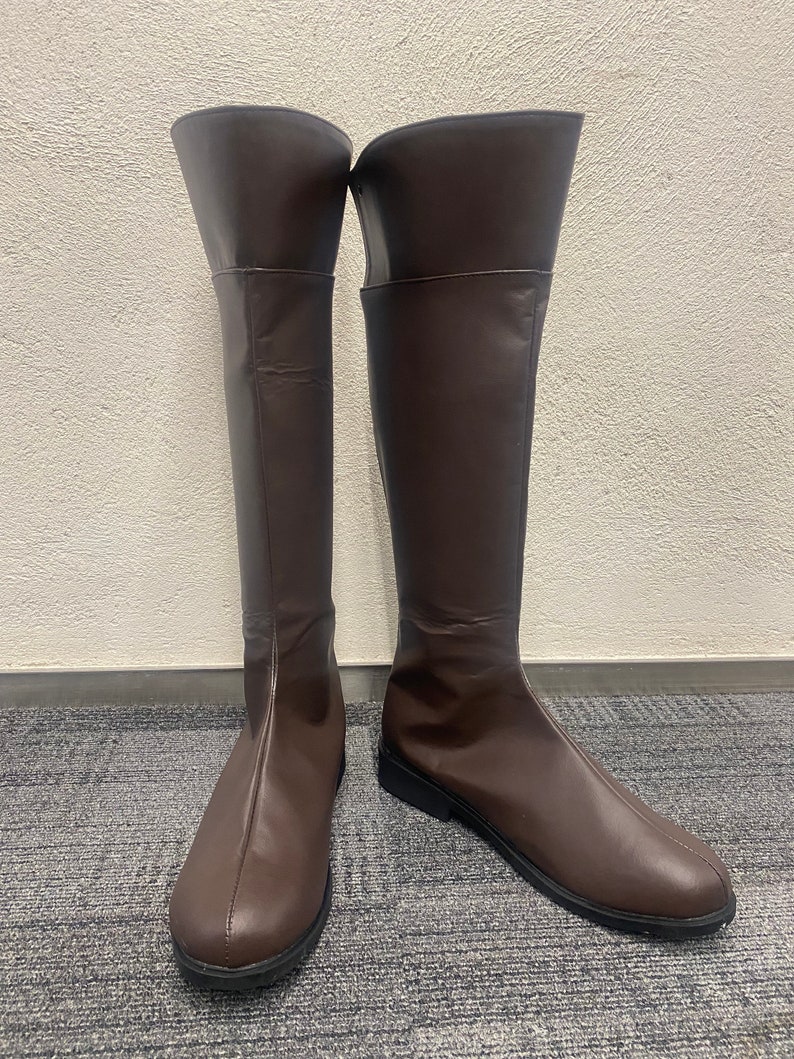 May include: A pair of brown leather knee-high boots with a rounded toe and a low heel.