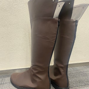 May include: A pair of brown leather knee-high boots with a zipper on the back. The boots have a pointed toe and a low heel.