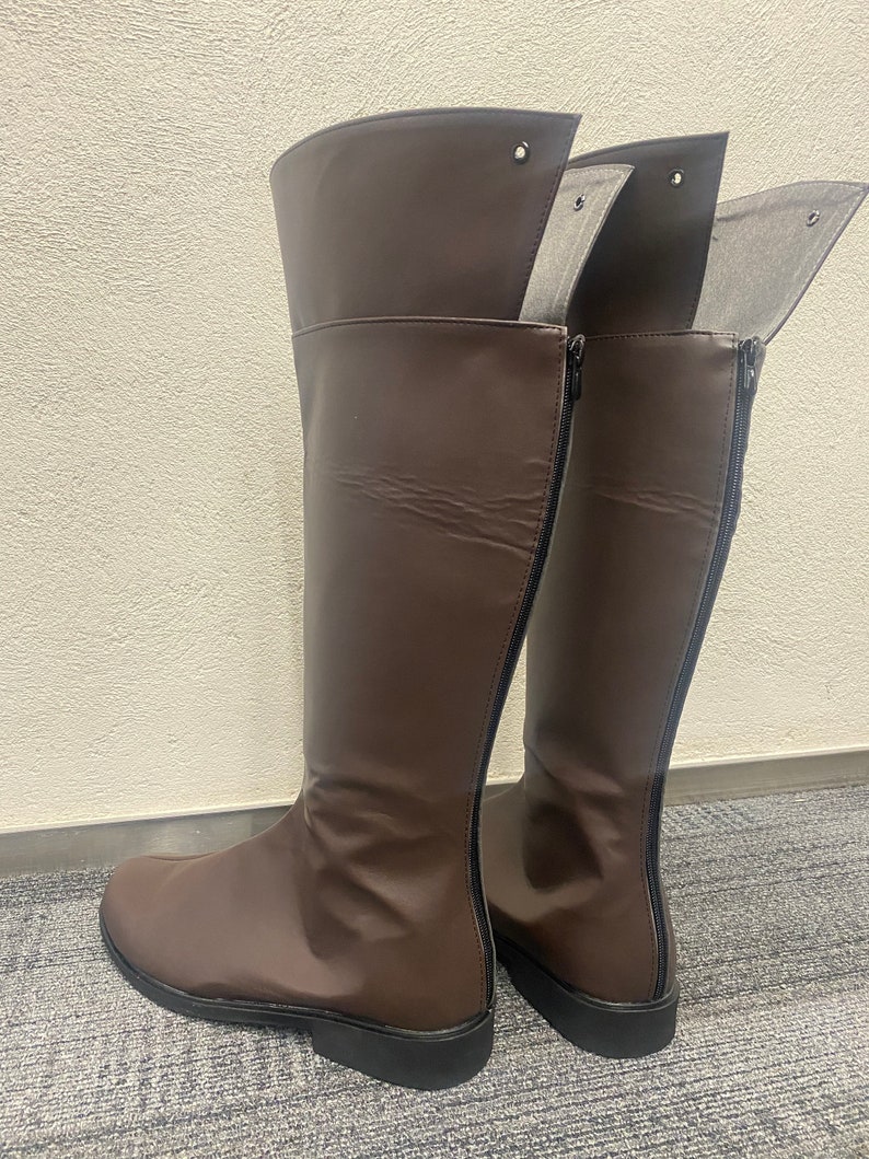 May include: A pair of brown leather knee-high boots with a zipper on the back. The boots have a pointed toe and a low heel.
