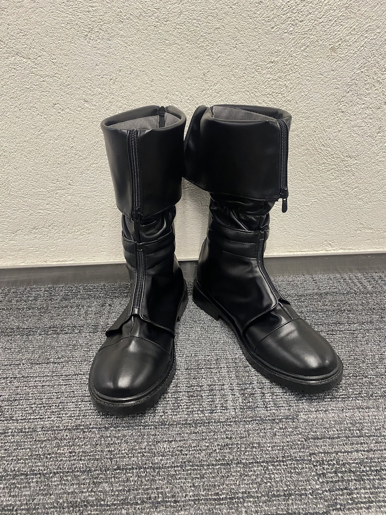 May include: A pair of black leather boots with a zipper up the front and a buckle strap. The boots have a rounded toe and a low heel.