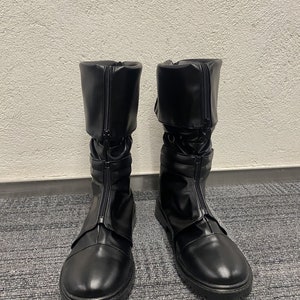 May include: A pair of black leather boots with a zipper up the front and a buckle strap around the ankle.