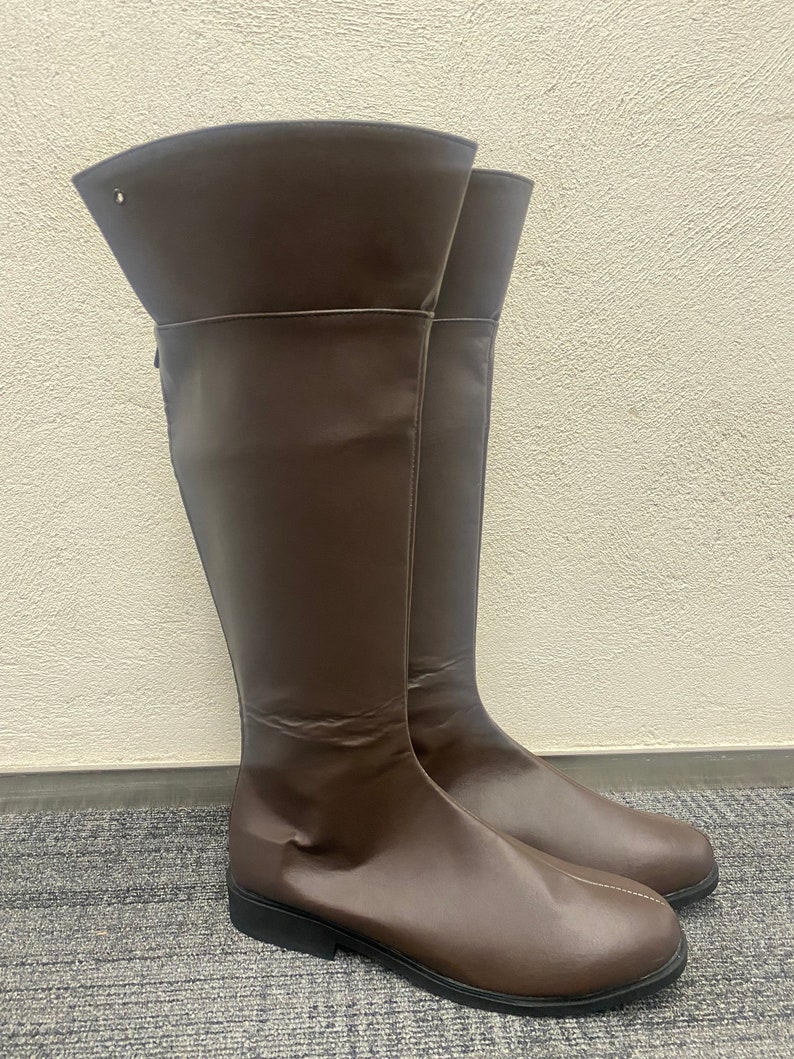 May include: A pair of brown leather knee-high boots with a pointed toe and a low heel.