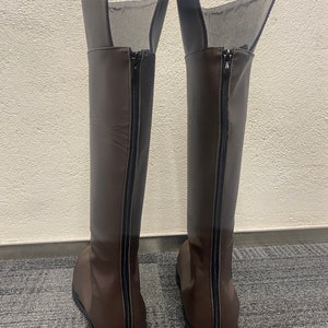 May include: A pair of brown leather knee-high boots with black zippers on the back.