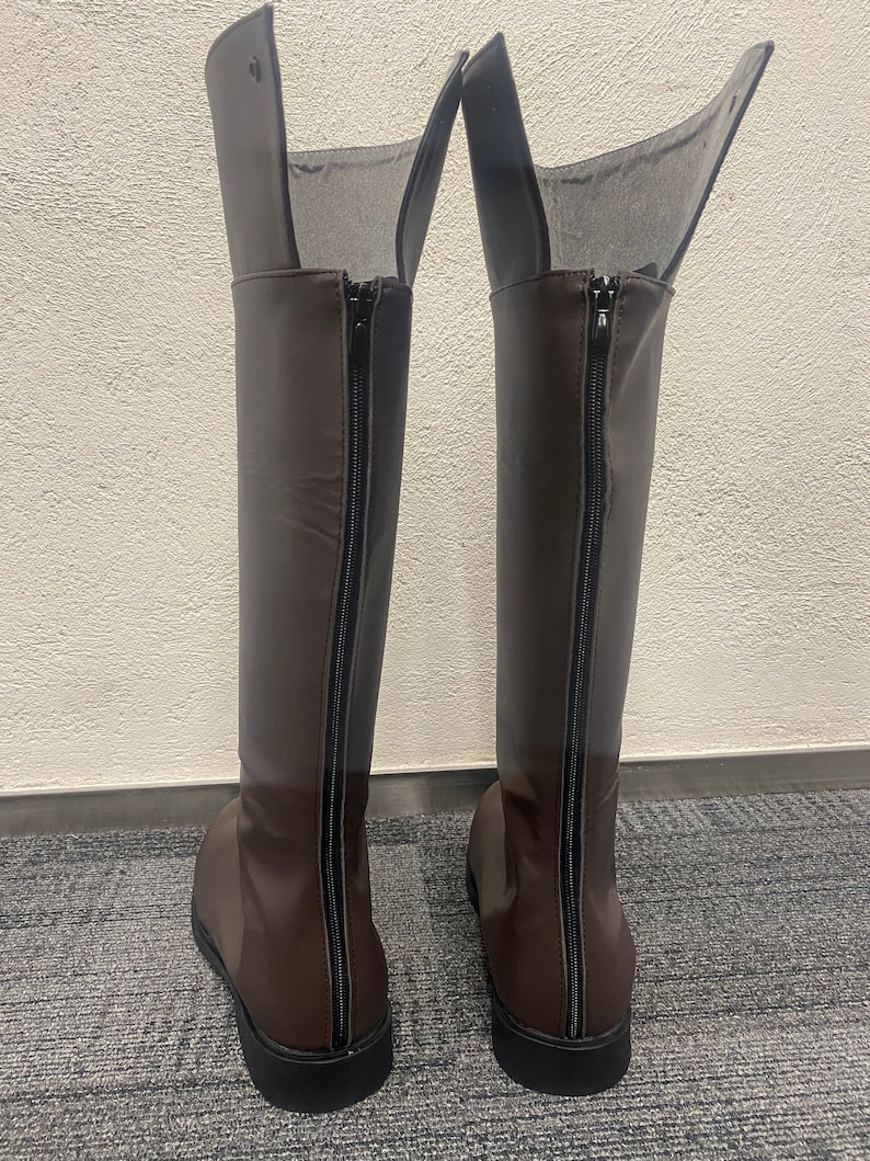 May include: A pair of brown leather knee-high boots with black zippers on the back.