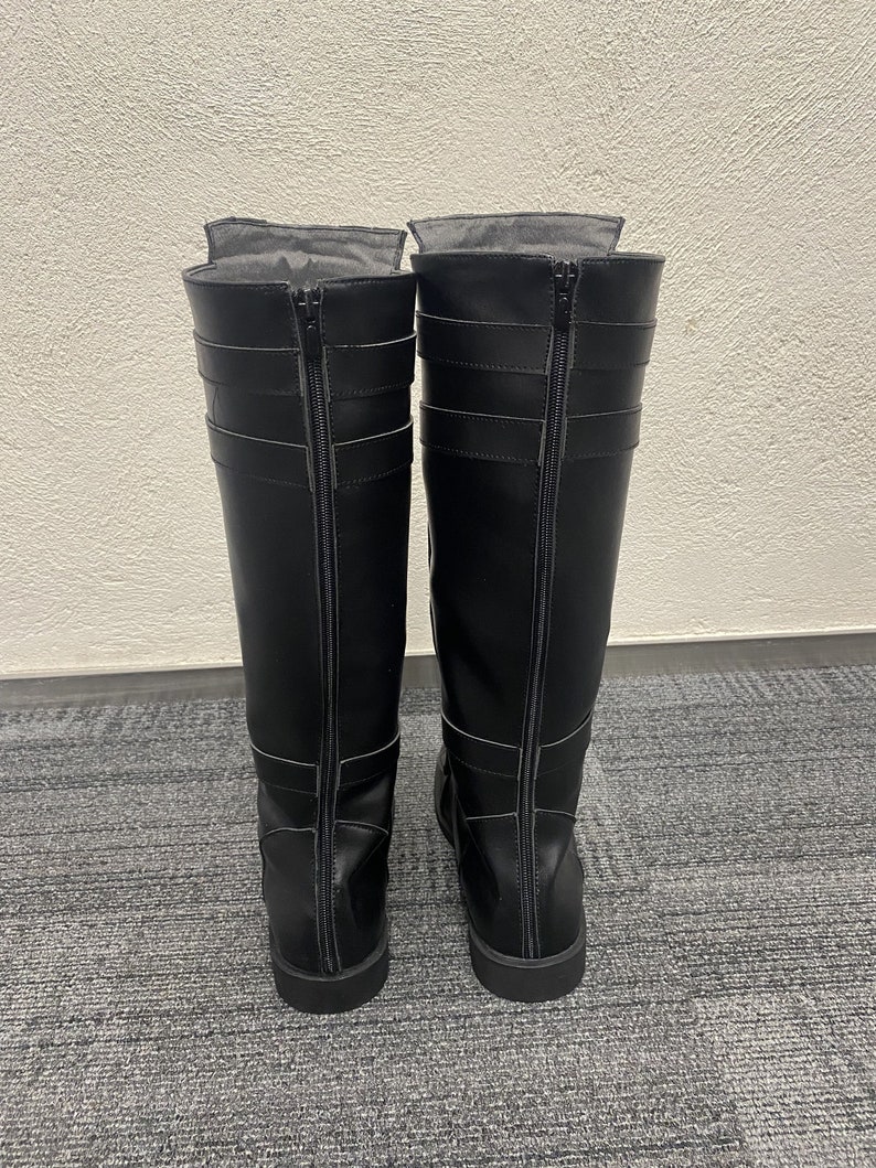 May include: A pair of black knee-high boots with zippers running down the back. The boots have multiple straps and buckles for a decorative touch. The boots are made of a smooth, leather-like material.