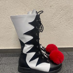Puede incluir: Botas negras y blancas de ca&ntilde;a alta con pompones rojos peludos. Las botas tienen un cierre de cordones en la parte delantera y una suela blanca.